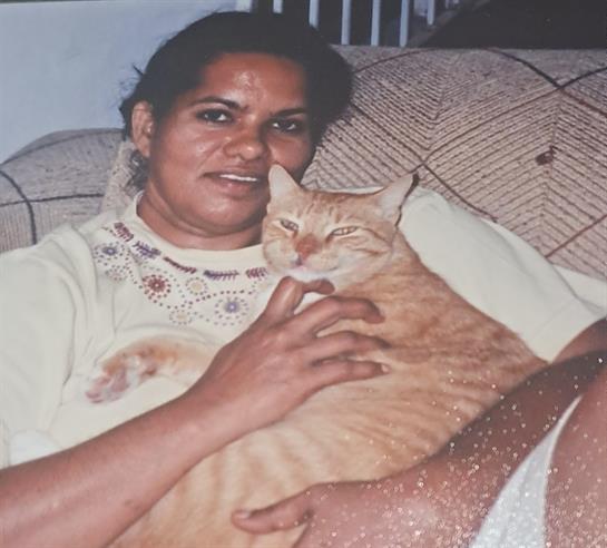 A woman sits comfortably on a couch holding her orange cat, both looking serene and relaxed.