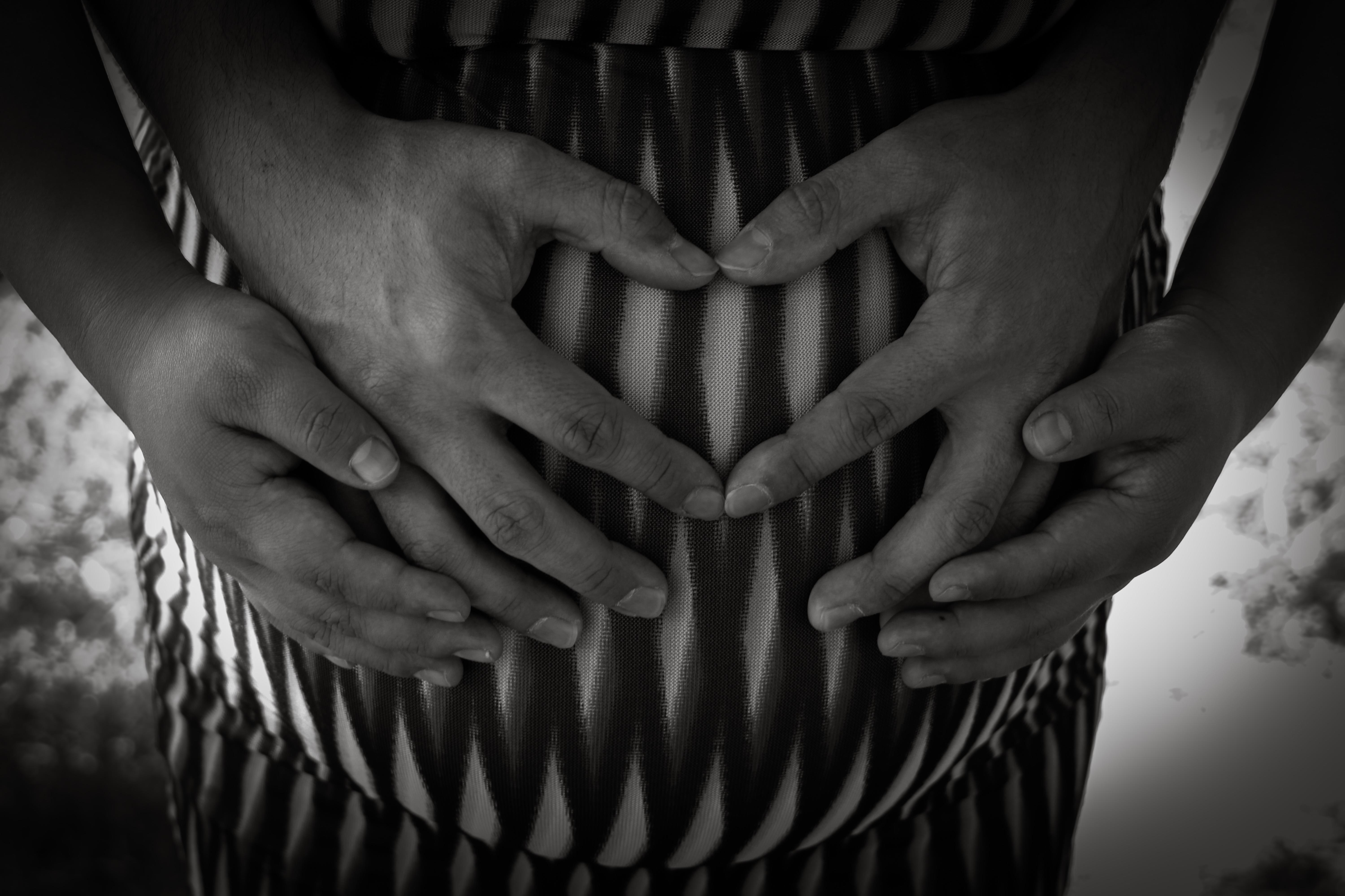 Two hands form a heart shape on a pregnant belly, symbolizing love and anticipation.