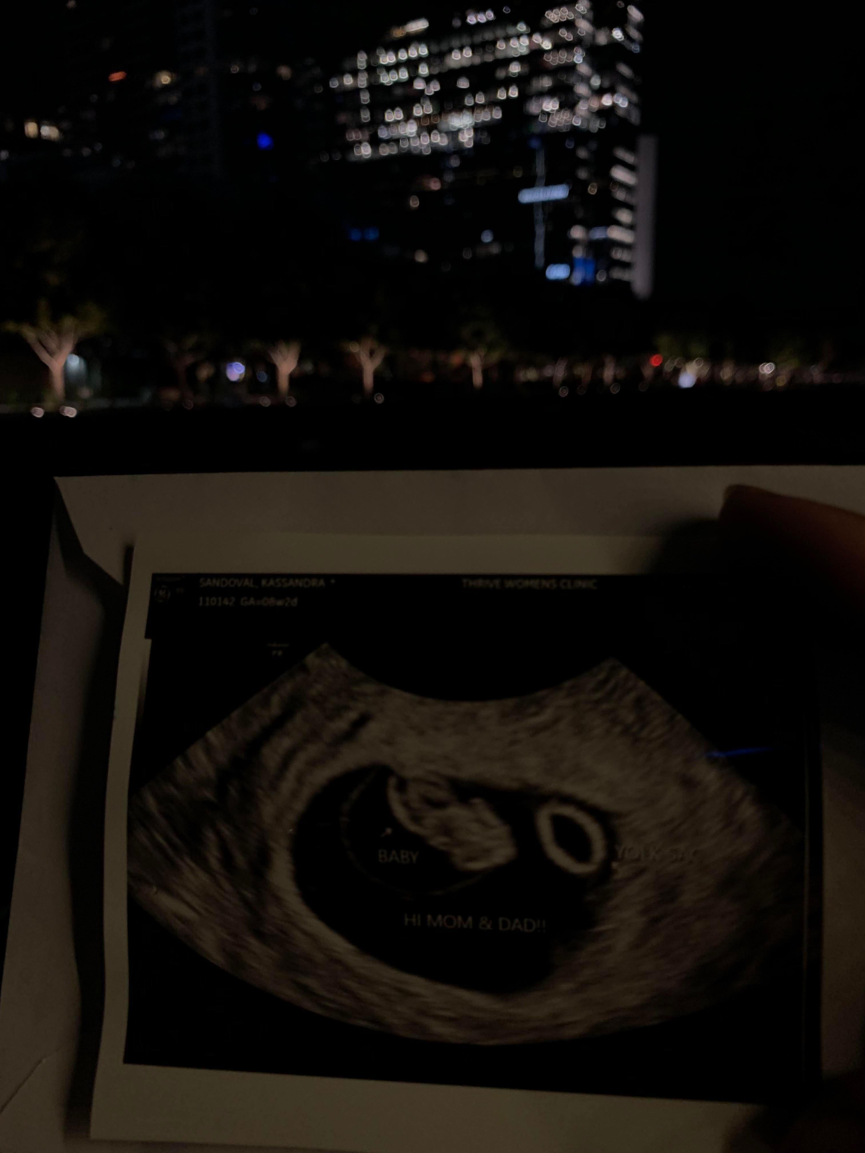 Parents eagerly share ultrasound image while enjoying the vibrant city atmosphere at night.