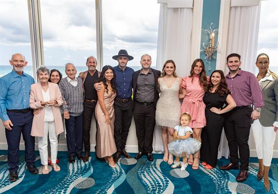 A joyful group of family members poses together in a coastal venue, celebrating a special day.