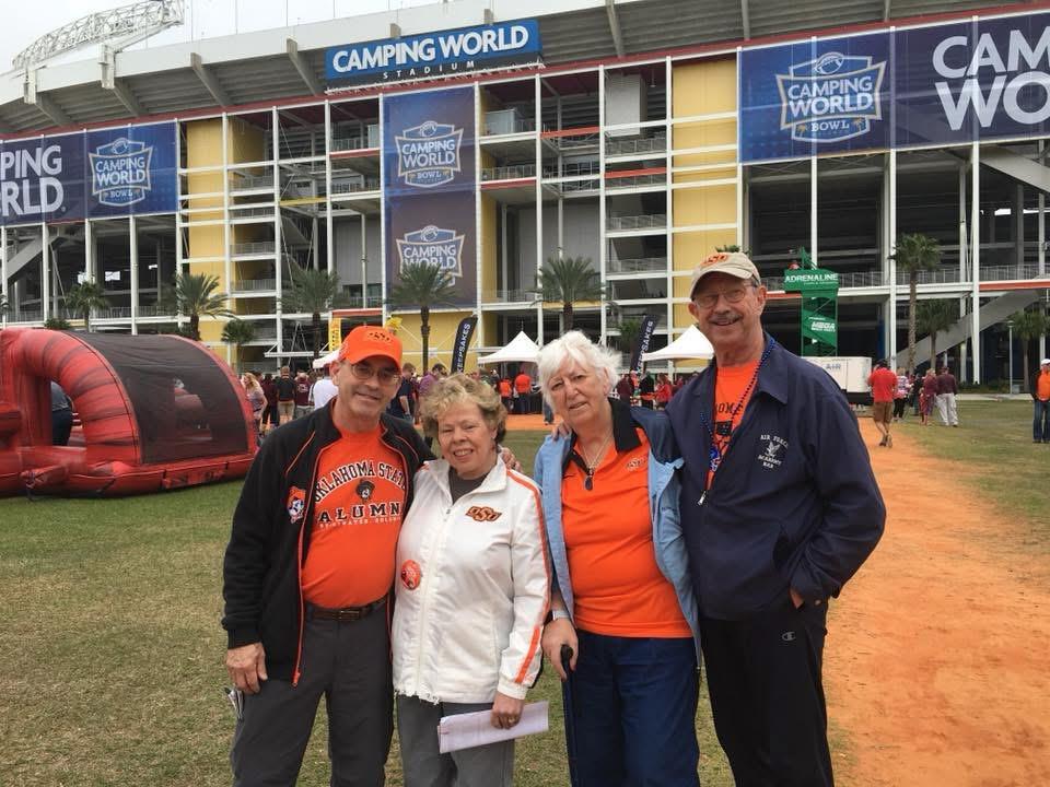 Friends gather wearing orange attire, enjoying an outdoor event at Camping World Stadium.
