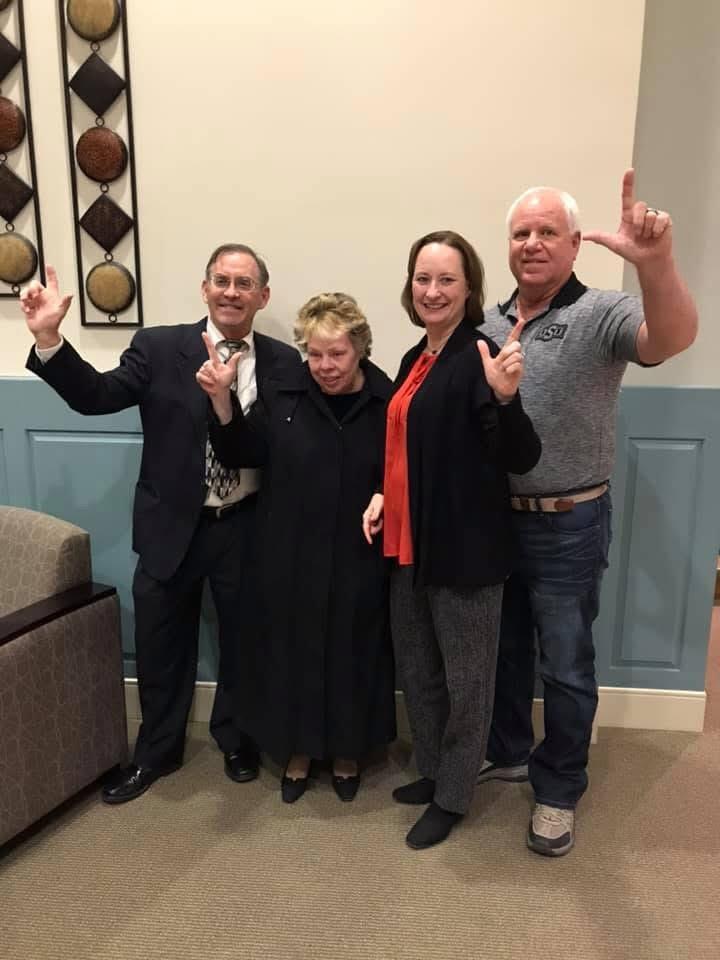 Four people pose happily in formal and casual attire, celebrating together in a warm atmosphere.