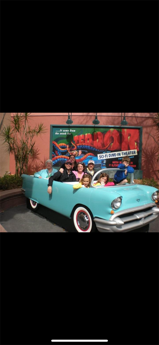 A lively group enjoys a fun moment together in a classic turquoise car at a theme park.