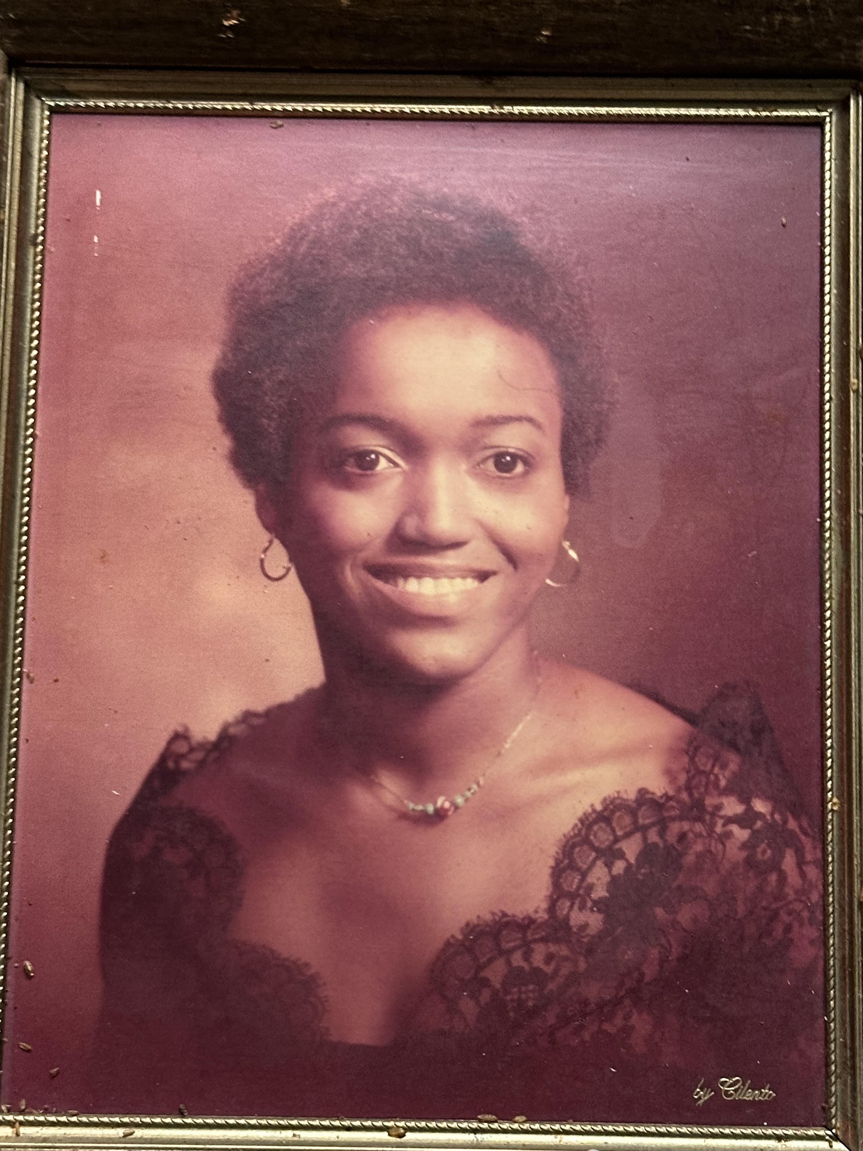 A woman poses gracefully, wearing a black lace dress and showcasing a warm smile.