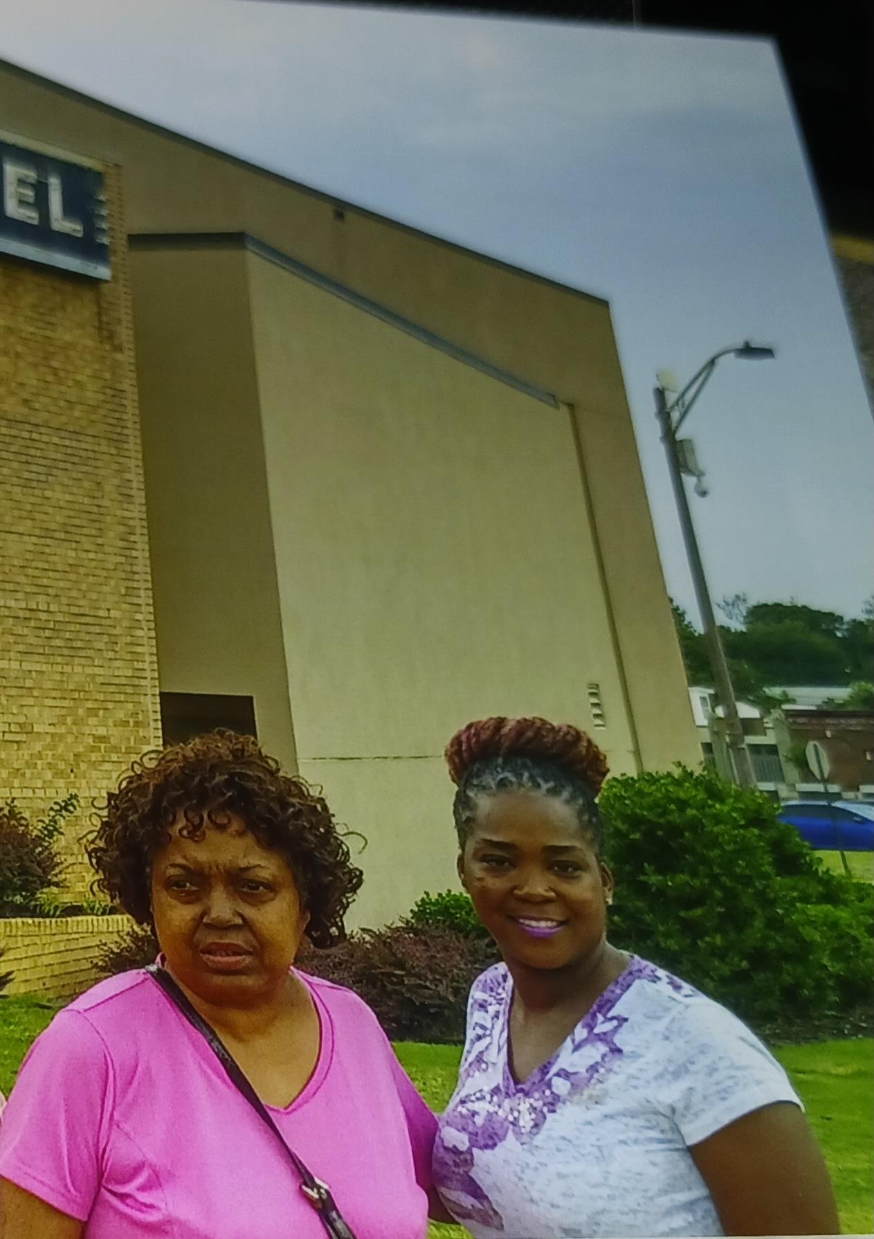 Two women pose outside a hotel, displaying various emotions against a cloudy backdrop.
