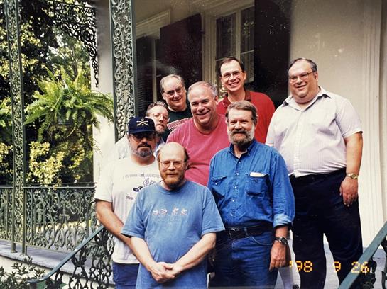 A group of eight friends poses together on a porch, smiling and enjoying the moment.