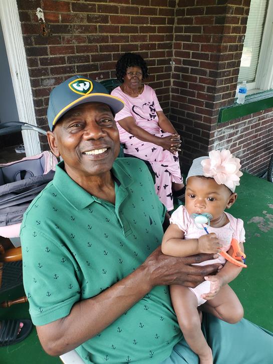 A man holding a baby and a woman sitting in front of a brick wall