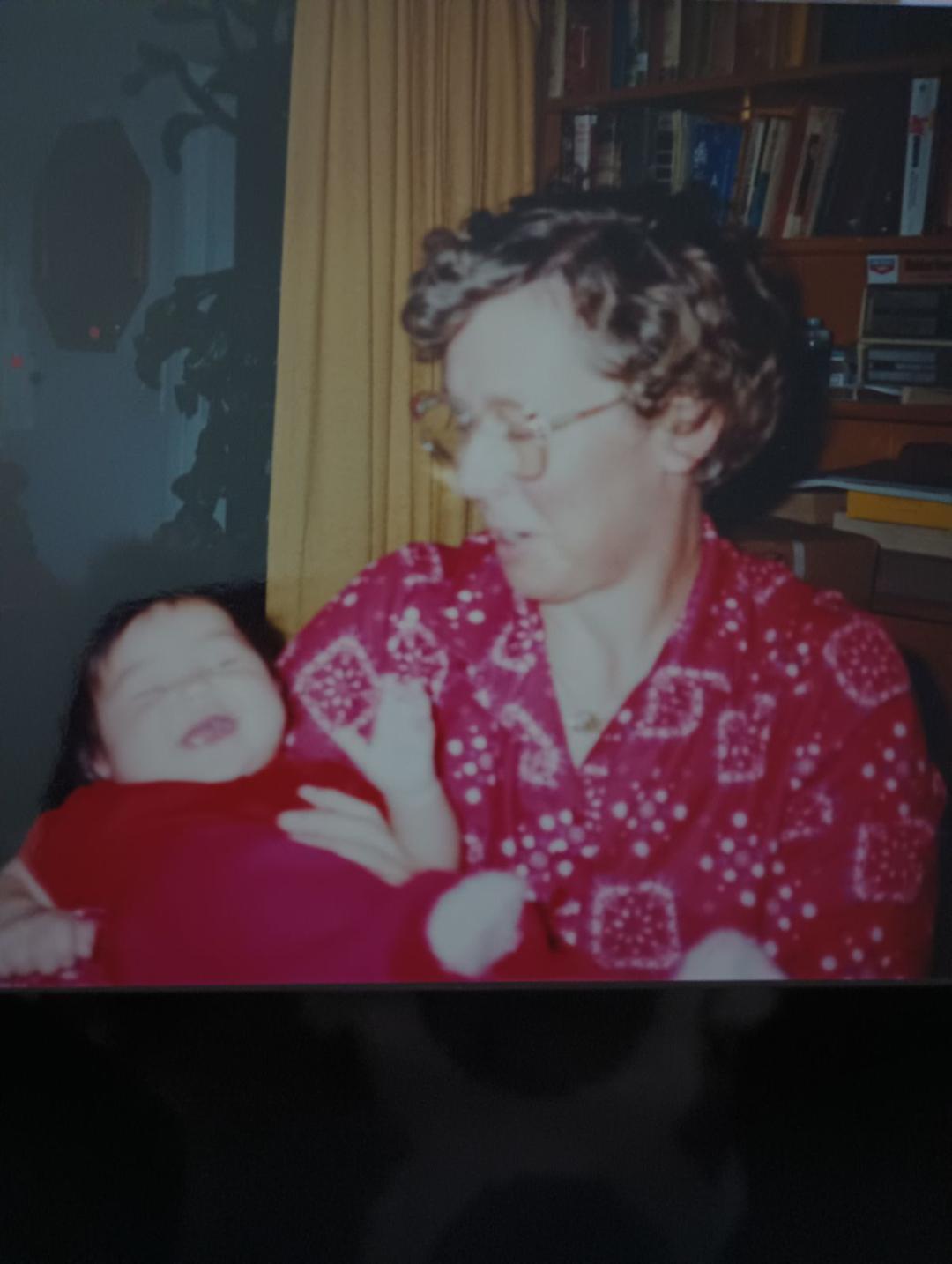 A joyful grandparent embraces a baby, both sharing a warm moment in a vintage living room.