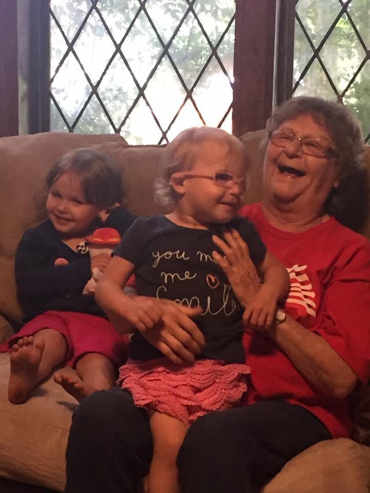 Smiling grandmother shares a joyful moment with her two delighted grandchildren on a couch.