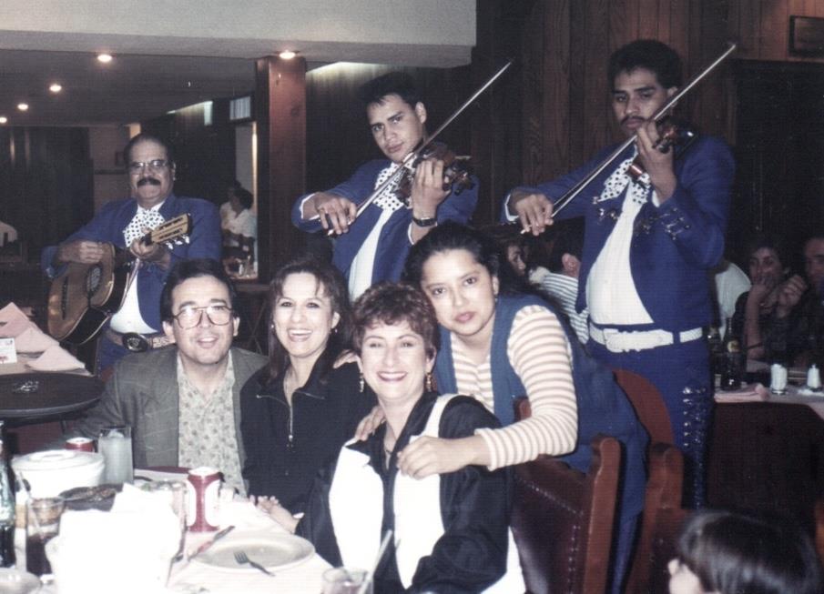 Friends and family gather at a bustling restaurant to enjoy dinner and live mariachi music.