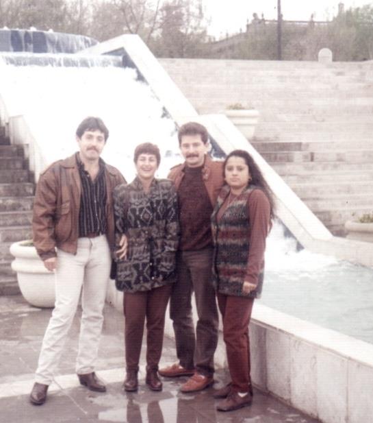 Friends gather for a memorable moment beside a fountain in a busy city park during autumn.
