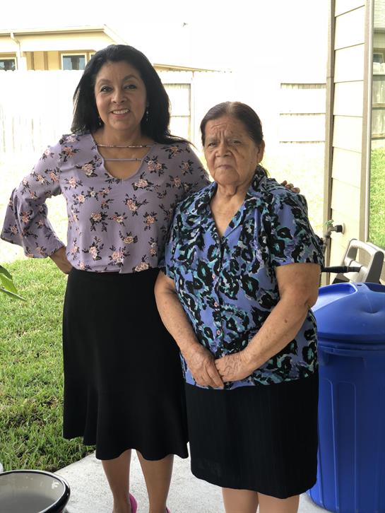 Two women smile gently while standing outside a house, enjoying each other's company.