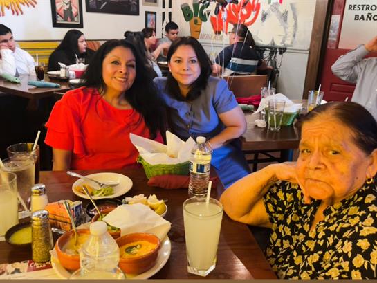 Three women dine at a table filled with colorful dishes and drinks, celebrating together.