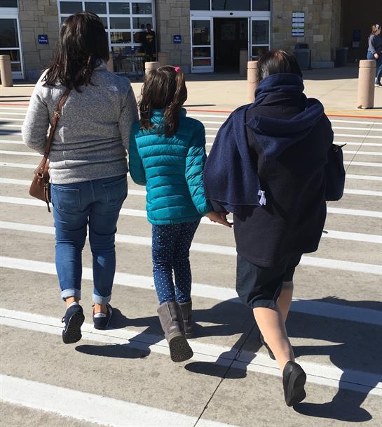 Three family members stroll hand in hand, crossing the parking lot on a sunny day.