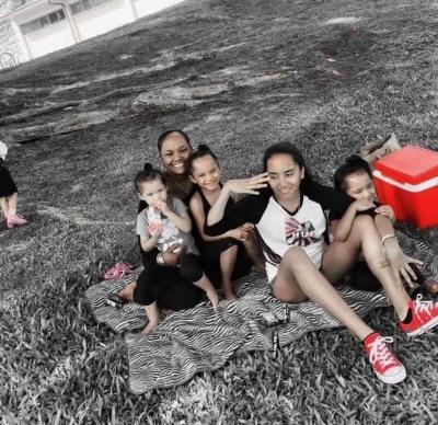 Five young people relax on a blanket, enjoying snacks and each other's company outdoors.