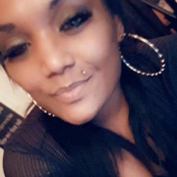 A woman with hoop earrings smiles warmly while chatting with friends indoors.