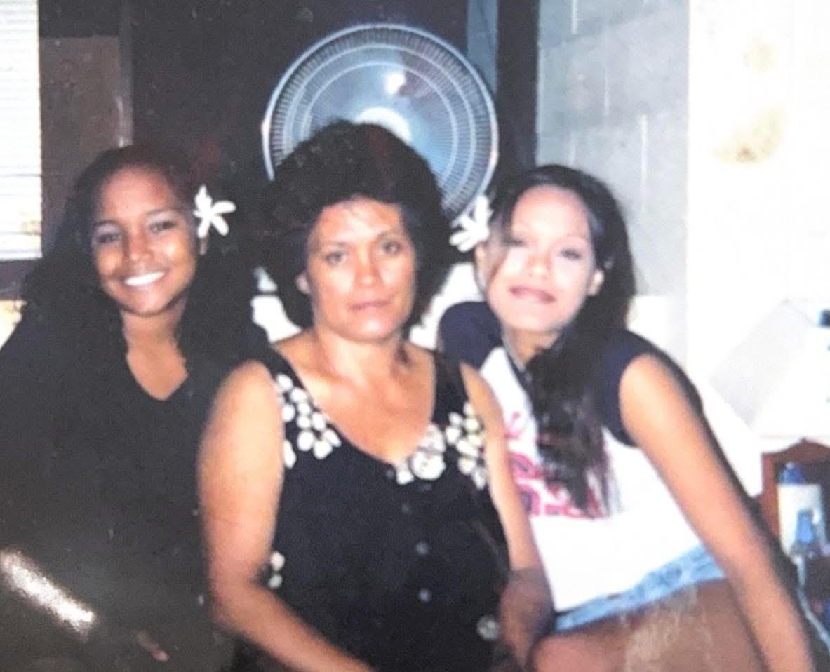 Three women pose closely together, sharing smiles and joy in a cozy indoor location at dusk.