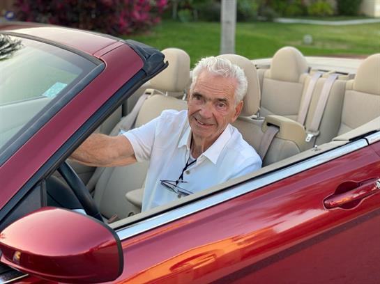A joyful senior man enjoys driving a red convertible with the top down on a bright day.
