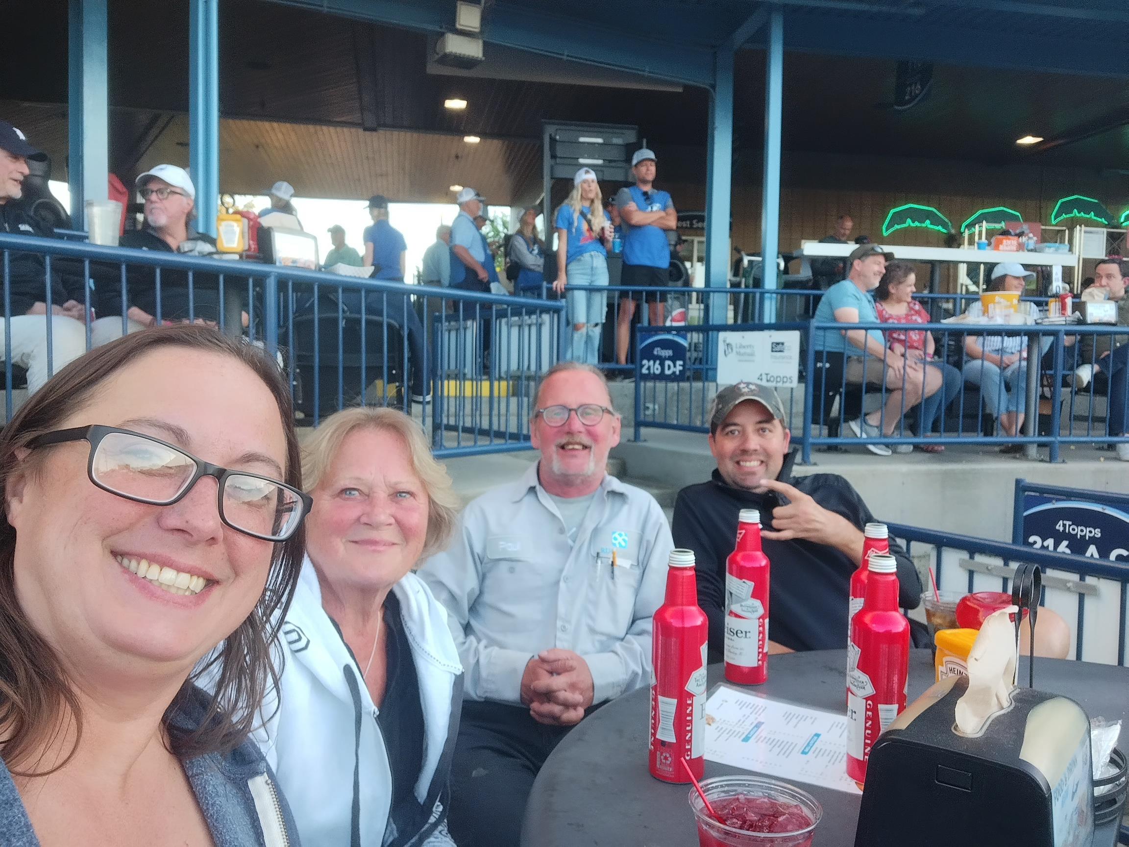 Group of friends smiling while sitting together at a baseball game, enjoying snacks and drinks.