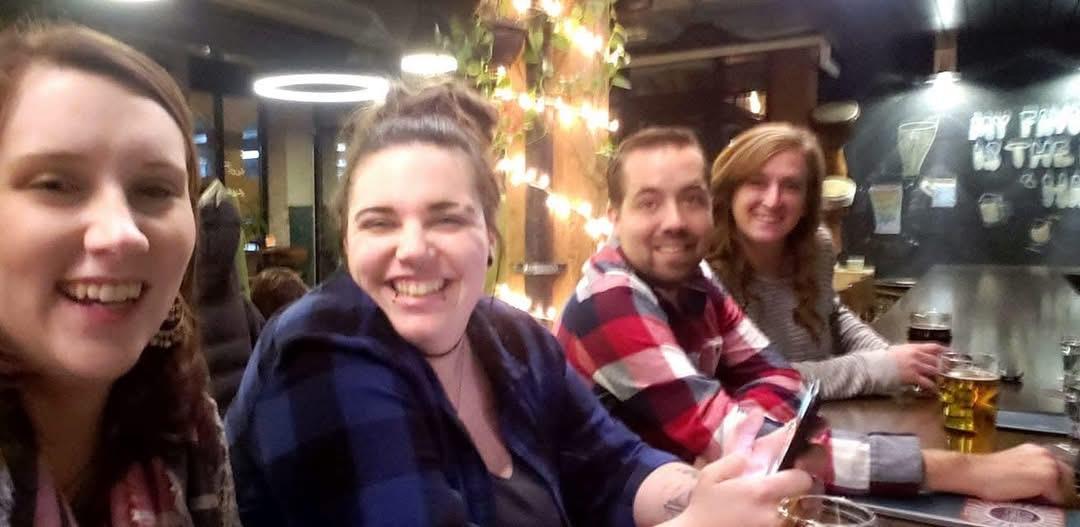 Friends smile and laugh while sitting at the bar, surrounded by warm, festive lights.