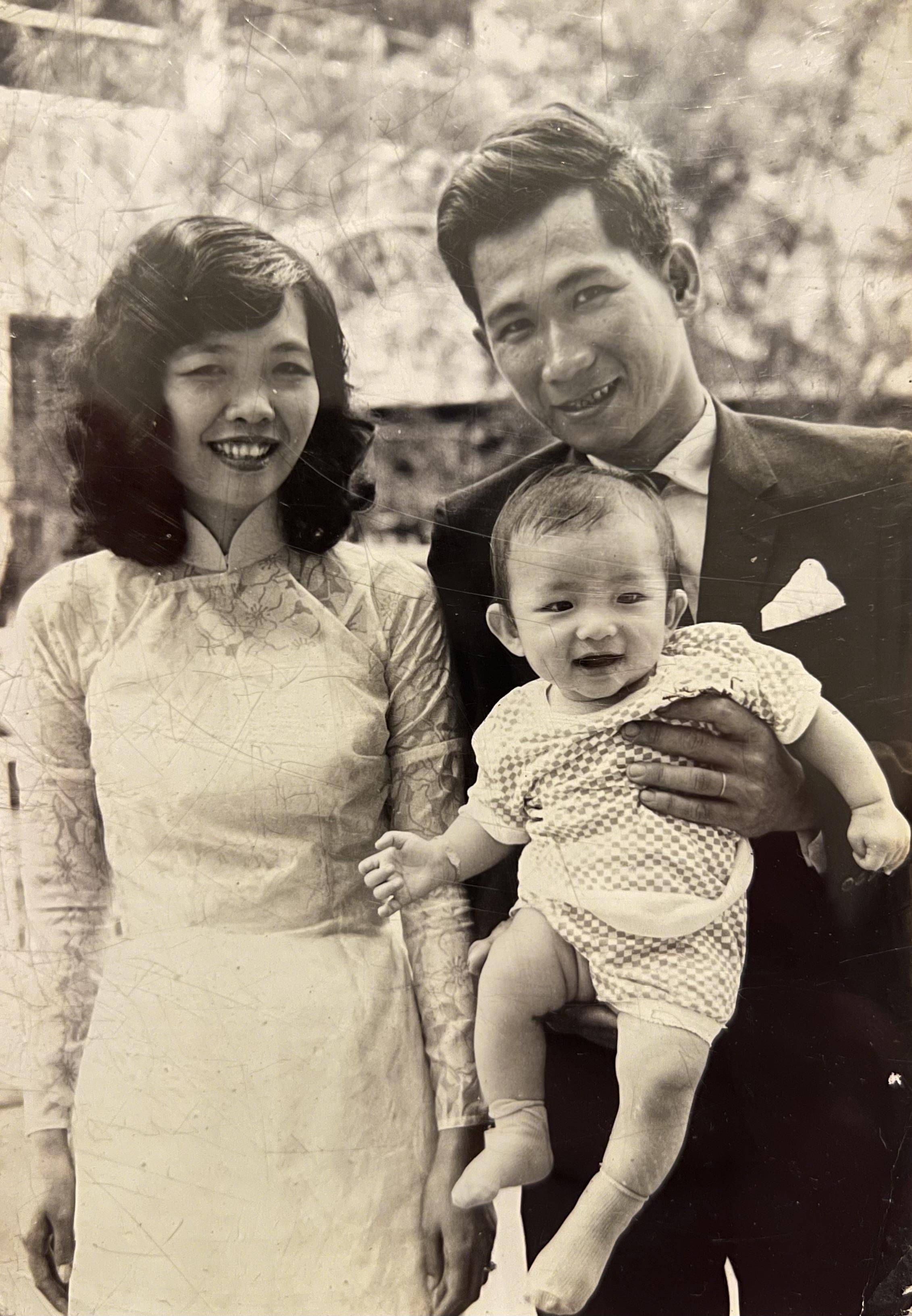 A couple stands with their happy baby in a garden, showcasing joy and family bonds.