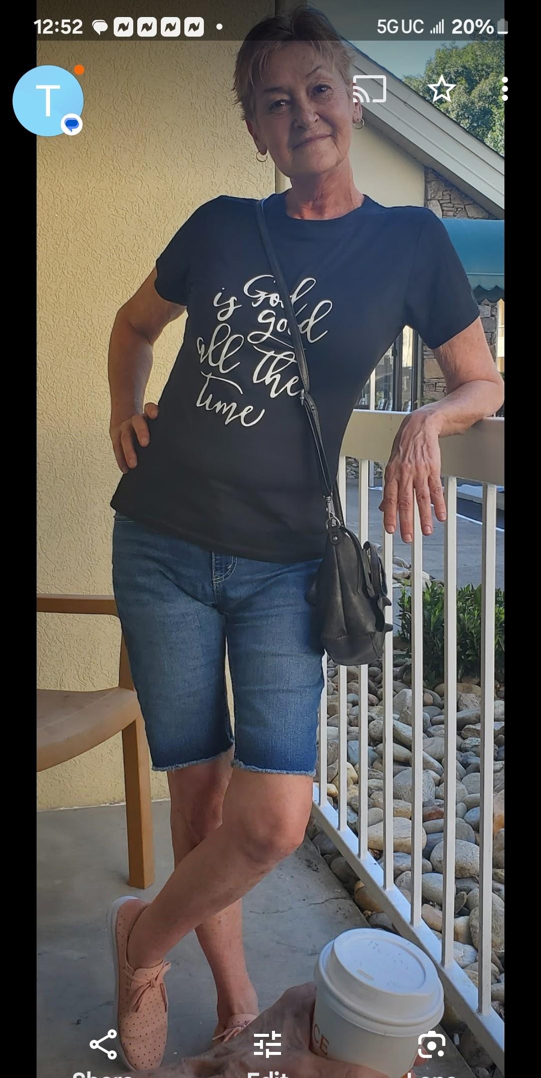 A woman wearing a trendy shirt and shorts leans against a railing with a relaxed expression.