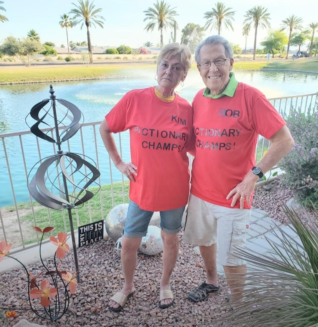 A happy couple in matching shirts stands by a calm pond, showing their championship spirit.