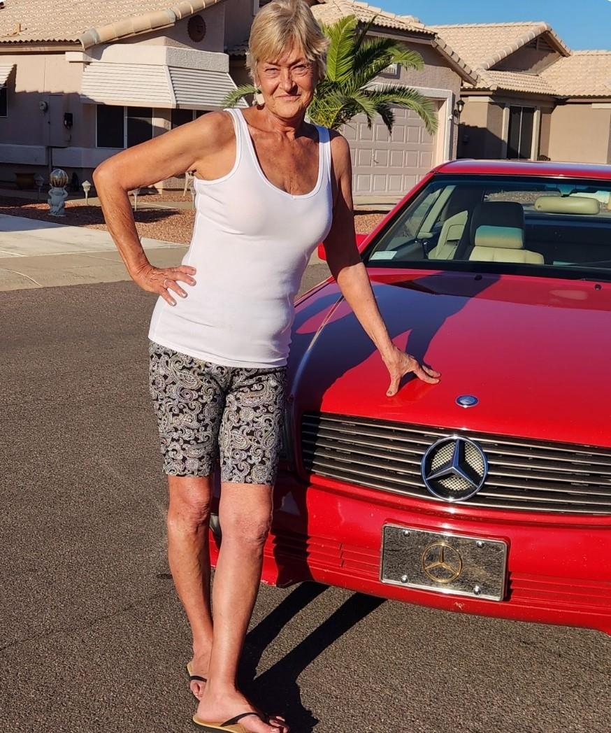 A woman stands proudly next to a bright red car, showcasing her confident demeanor.