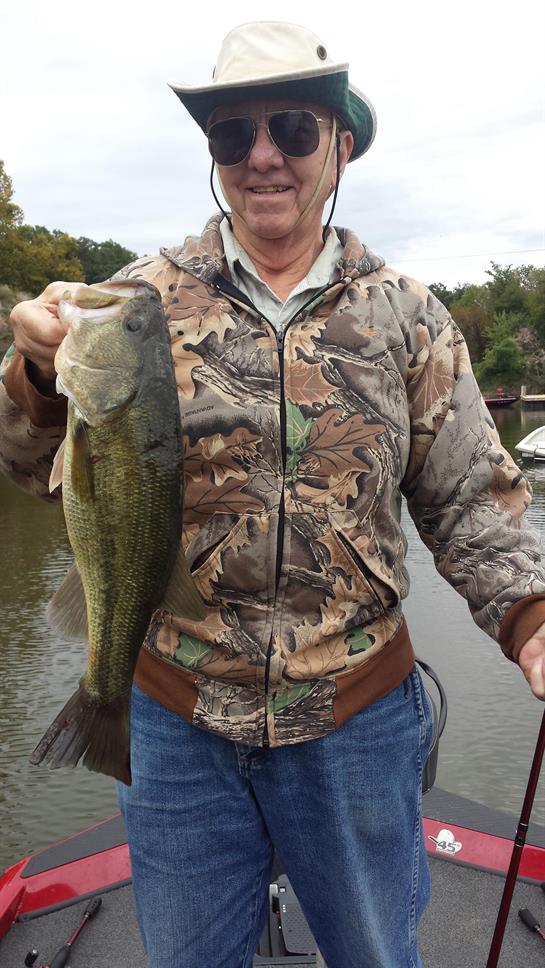 Individual proudly displays a large bass fish caught from a boat on a peaceful lake.