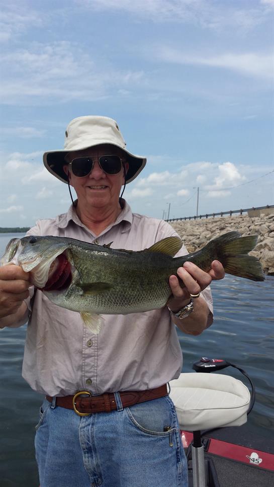 A fisherman proudly displays a large bass he caught on a lake during a sunny day.