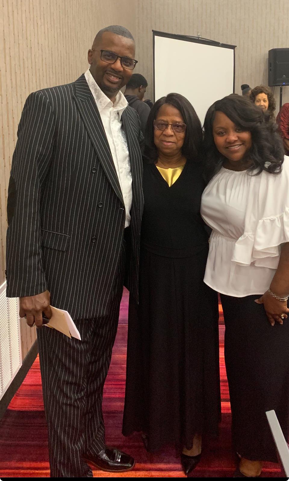 Three people smile together, showcasing a moment of joy at a formal event in a venue.
