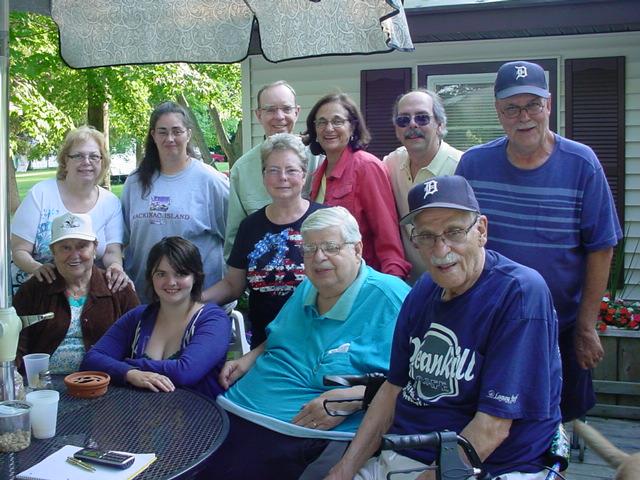 A group of cheerful individuals gather around a table in a backyard, sharing laughs and stories.