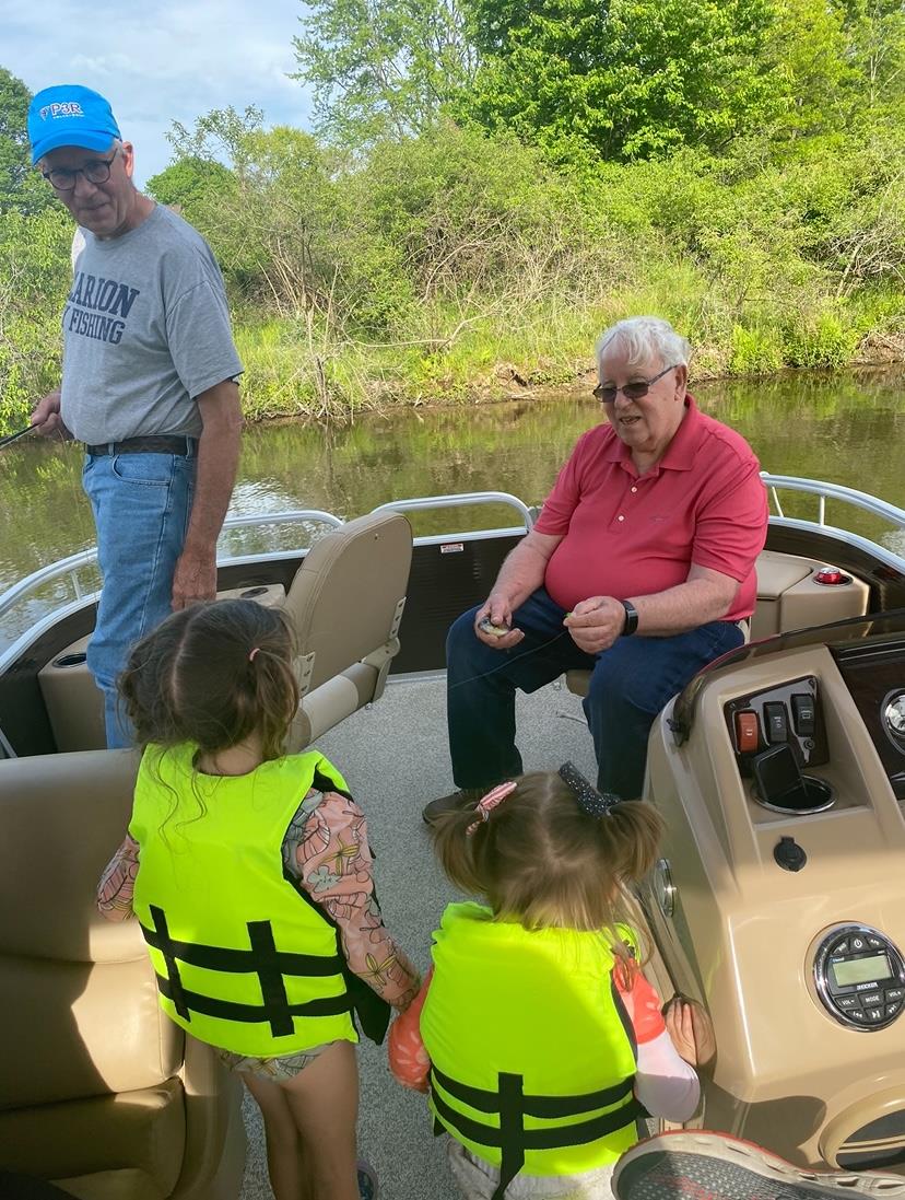 Two children in life jackets listen intently to an elder while boating on a river.