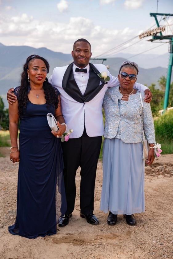 A stylish man poses with two women in a joyful celebration amid stunning mountain scenery.