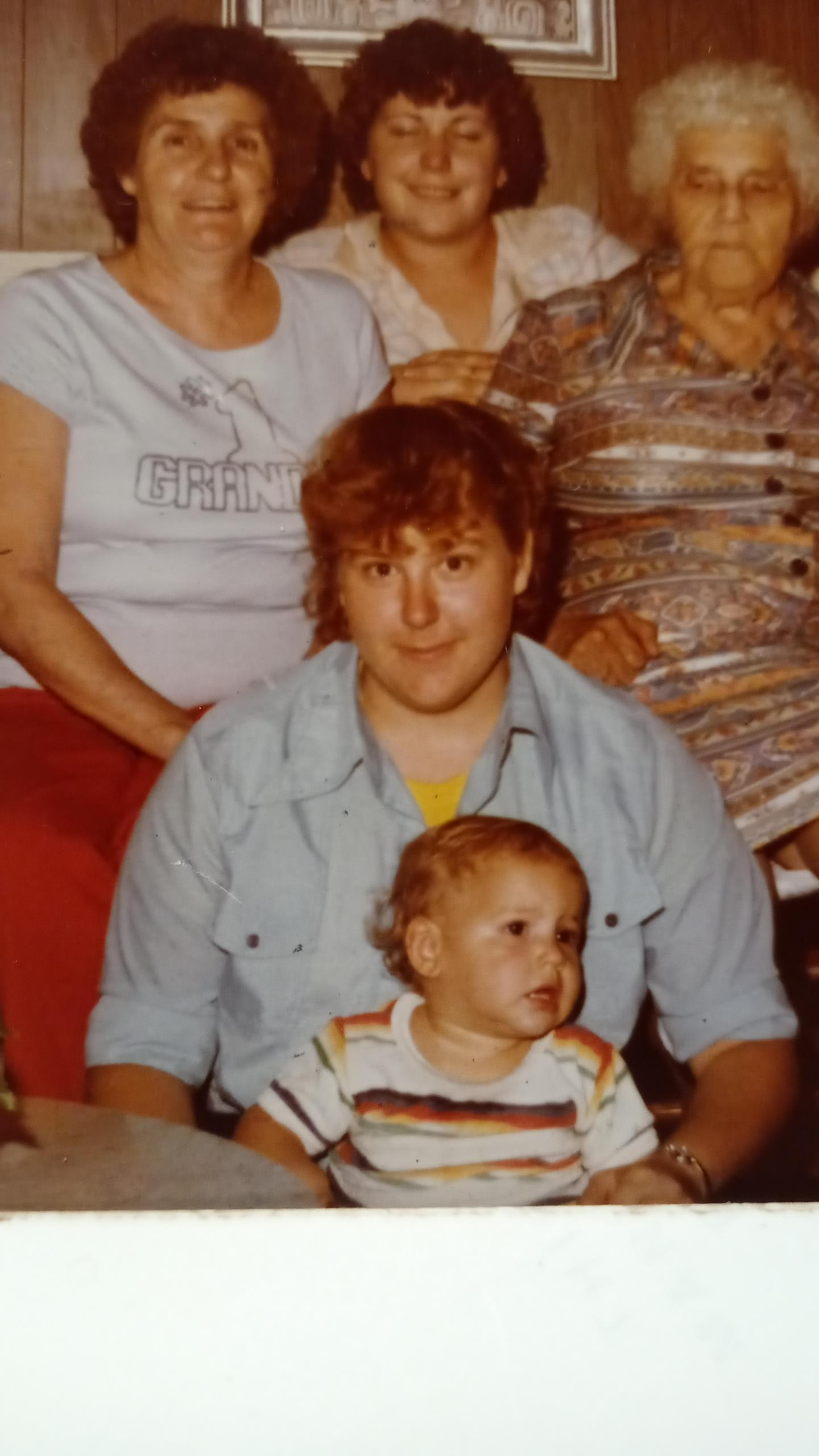 A young child sits on a person's lap, surrounded by family members, evoking warmth and nostalgia.