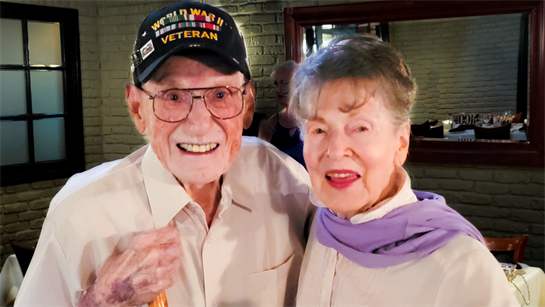 An elderly couple smiles broadly while enjoying a special moment at a restaurant gathering.