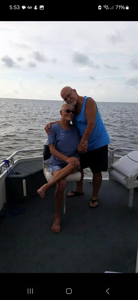 Two friends enjoy a relaxed moment on a sailboat, smiling and posing together by the water.