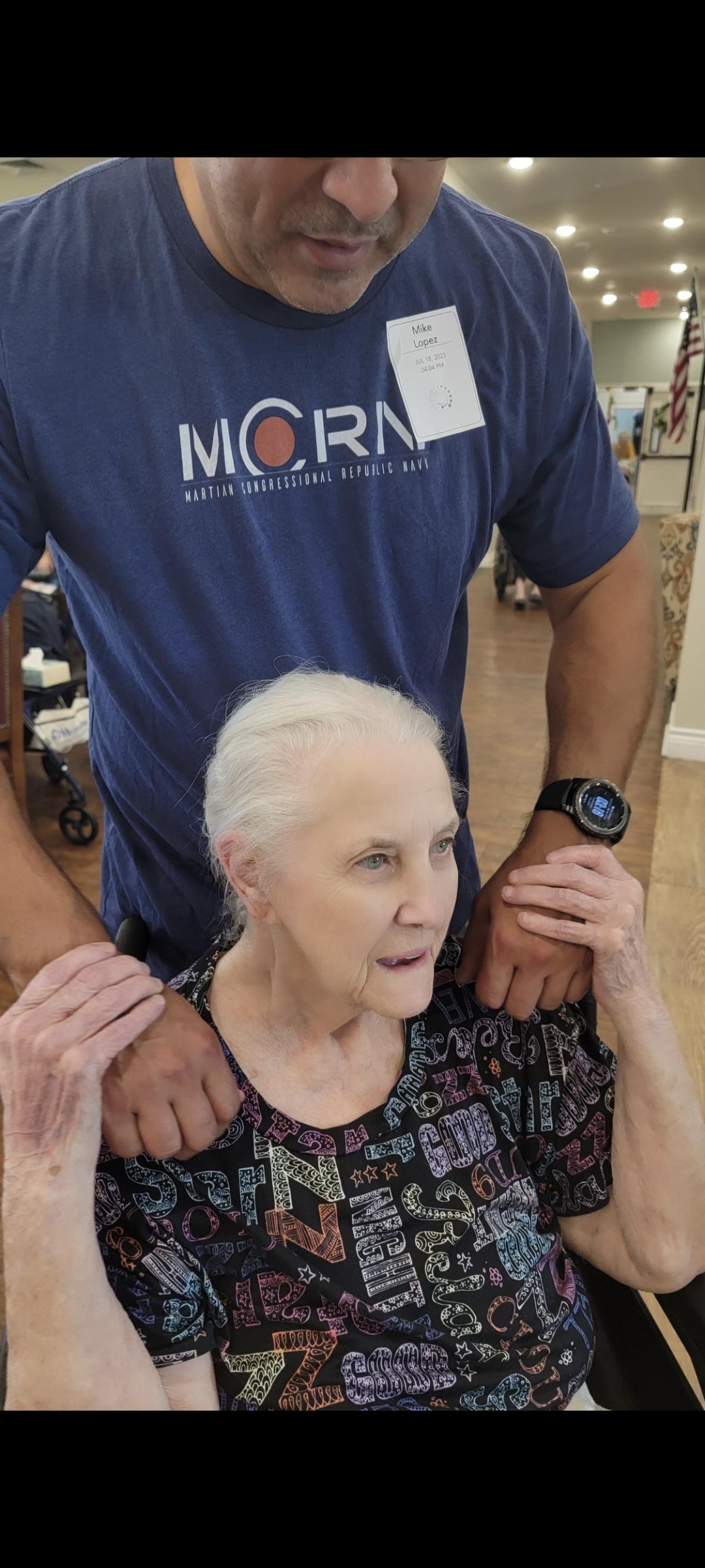A caregiver offers a shoulder massage to an elderly woman while engaging in a relaxing activity.
