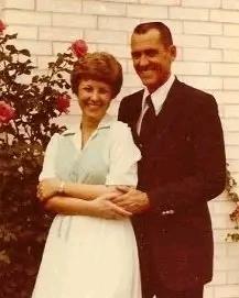 A joyful couple stands close together, smiling warmly, surrounded by vibrant roses.