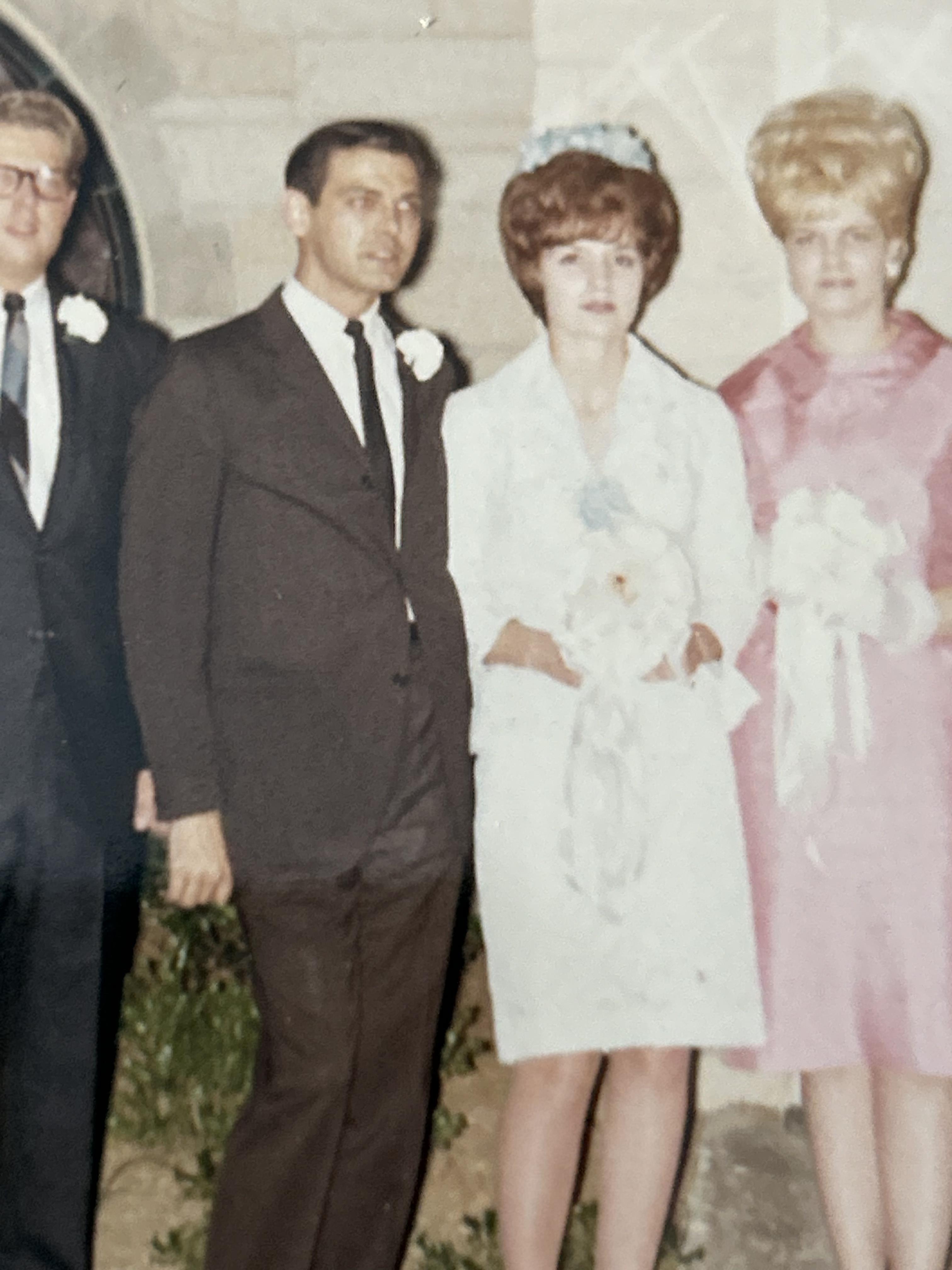 A couple in wedding attire poses with three guests outside a building, celebrating their union.