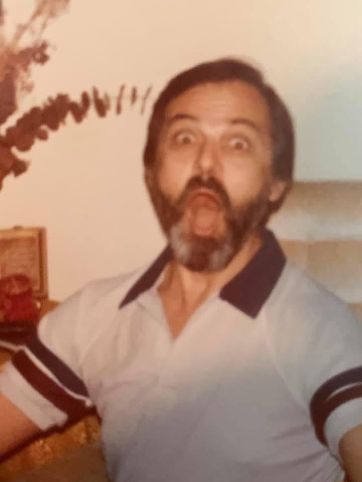 Older man shows a playful, surprised expression in a colorful room filled with decor.