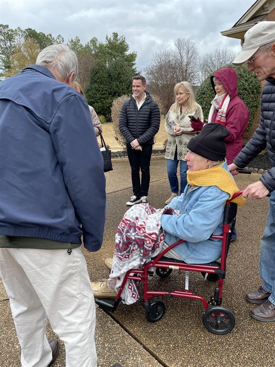 A woman in a wheelchair is surrounded by friends and family on a cool day outside.