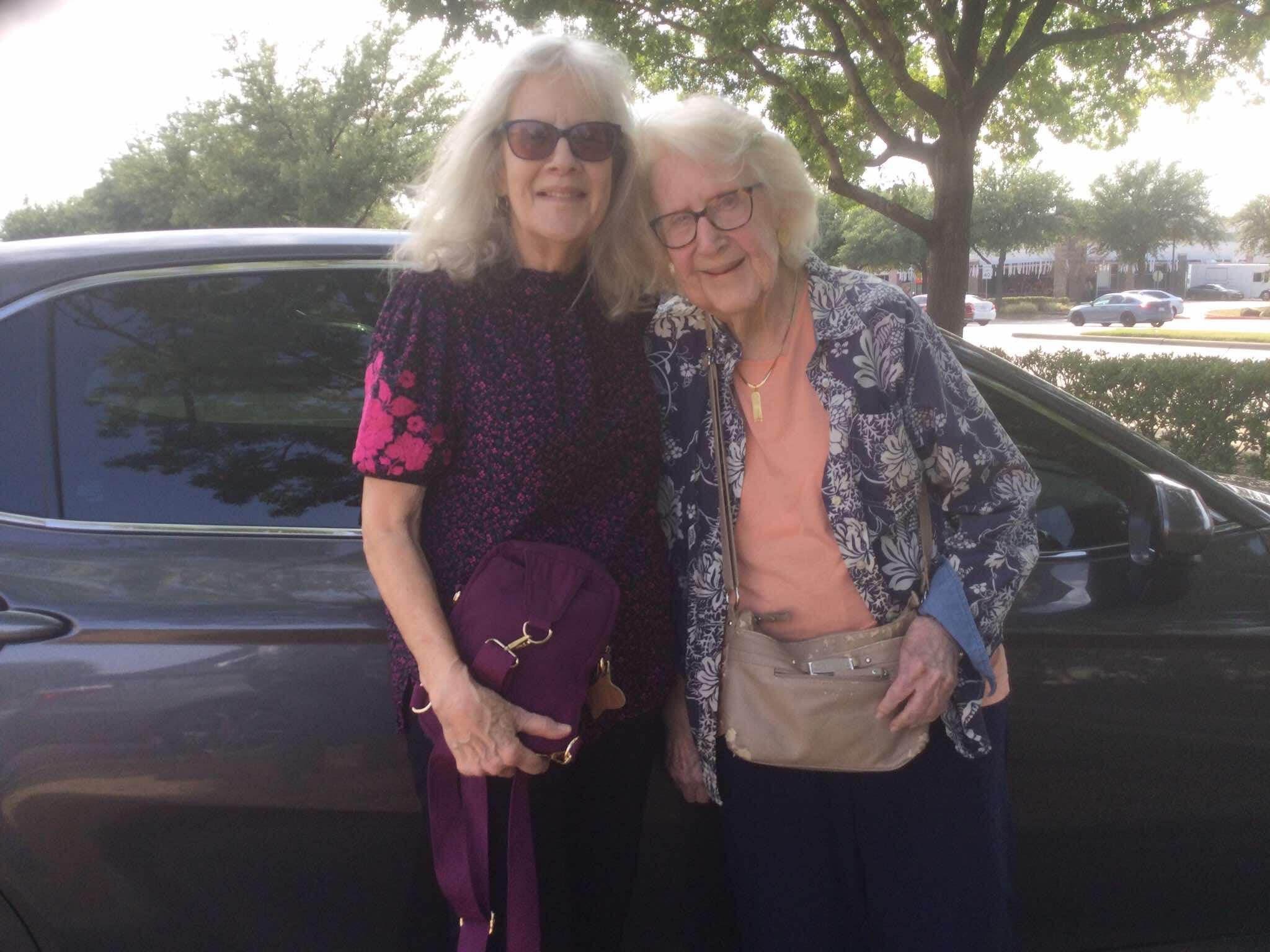 Two smiling elderly women pose cheerfully together, enjoying their day out in the sun.