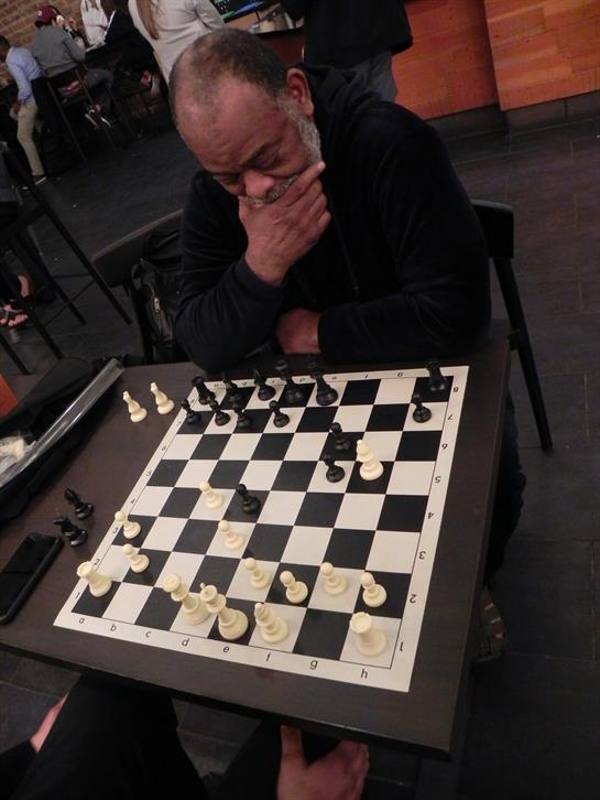 A man contemplates his next move while playing chess at a bustling cafe setting.