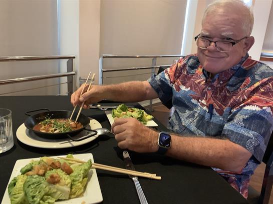 A man is savoring a tasty meal with chopsticks at a restaurant table in a relaxed atmosphere.