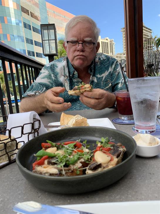 A man is enjoying a tasty dish at an outdoor restaurant table while holding a sandwich.
