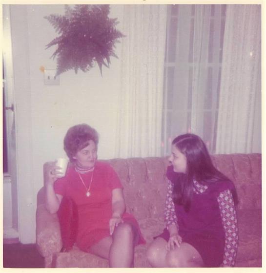 A woman sitting on a couch with another woman holding a cup