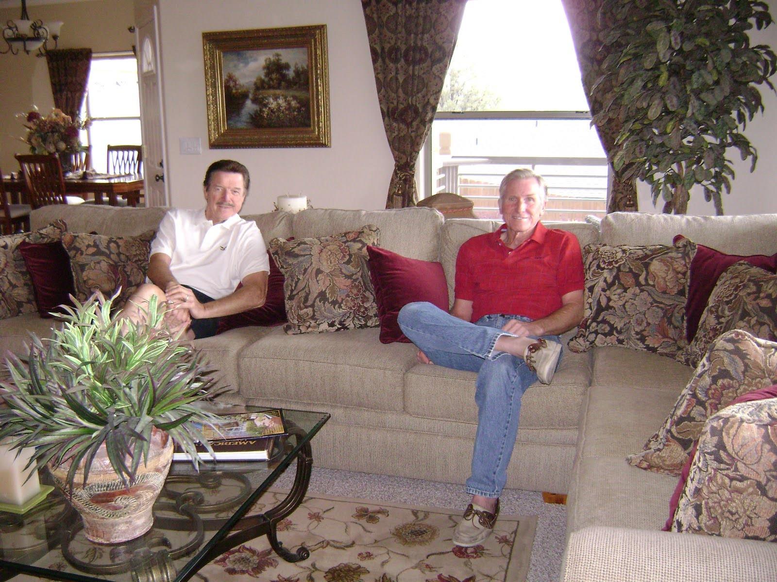Two men sit comfortably on a large couch in a stylish living room, enjoying each other's company.