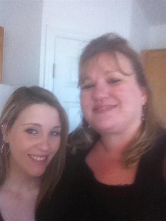 Two women share laughter and joy while posing closely in a bright kitchen.