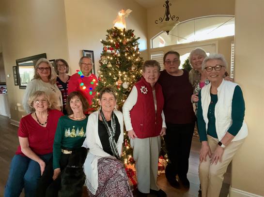 Friends happily pose by a beautifully decorated Christmas tree in a cozy living room.